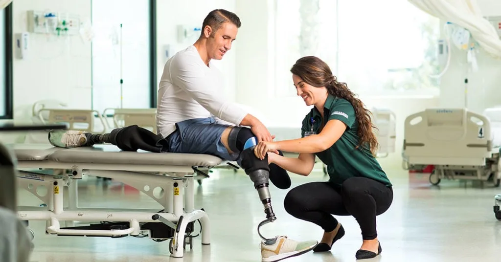 A therapist working with a patient fitting a prosthetic leg in a hospital rehabilitation gym